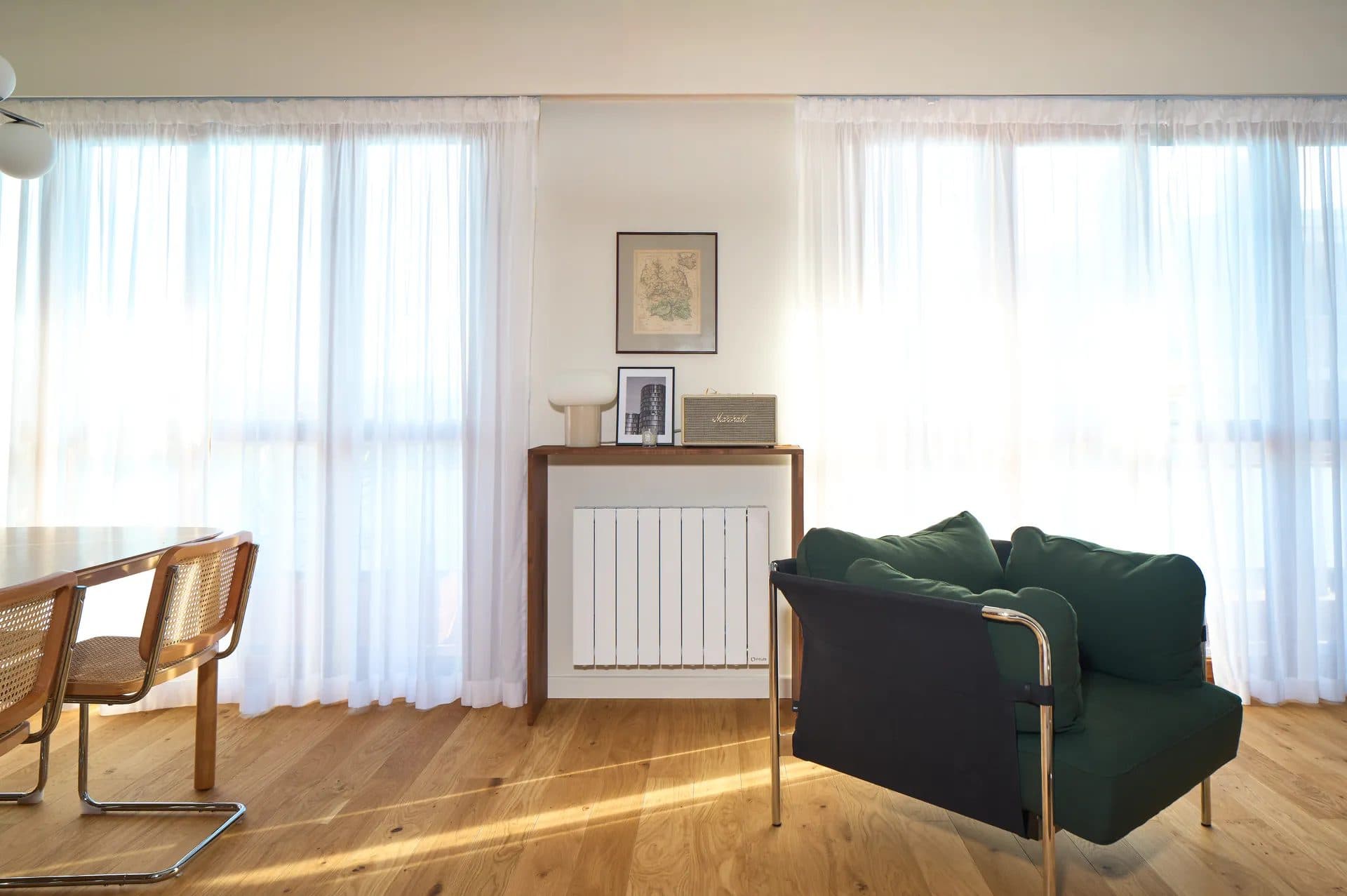 Chambre aux rideaux clairs, fauteuil en cuir et canapé vert sapin sur parquet