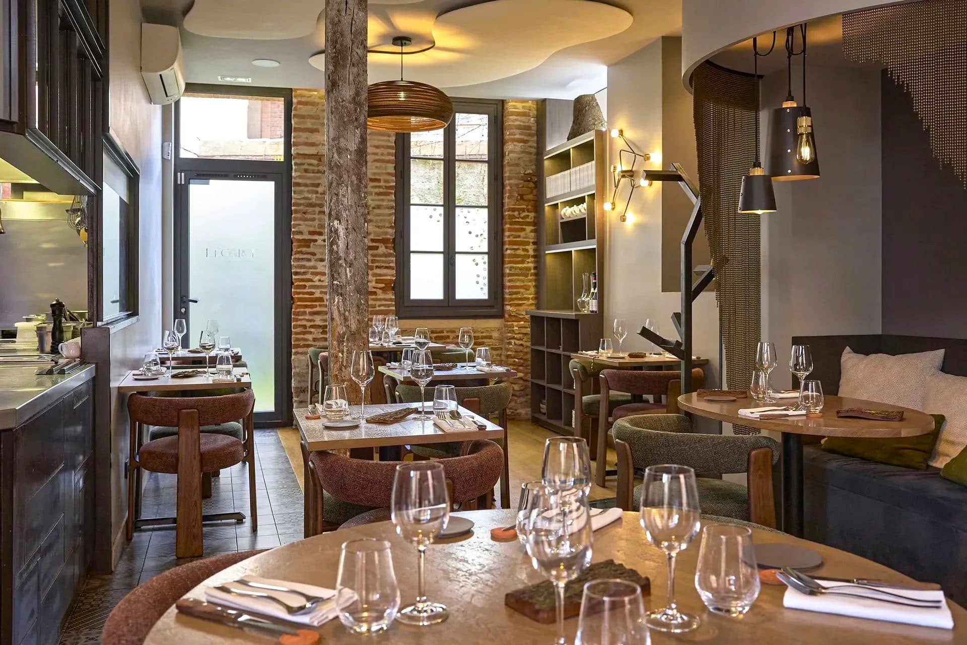 Salle de restaurant avec tables rondes en bois, brique apparente et suspensions noires