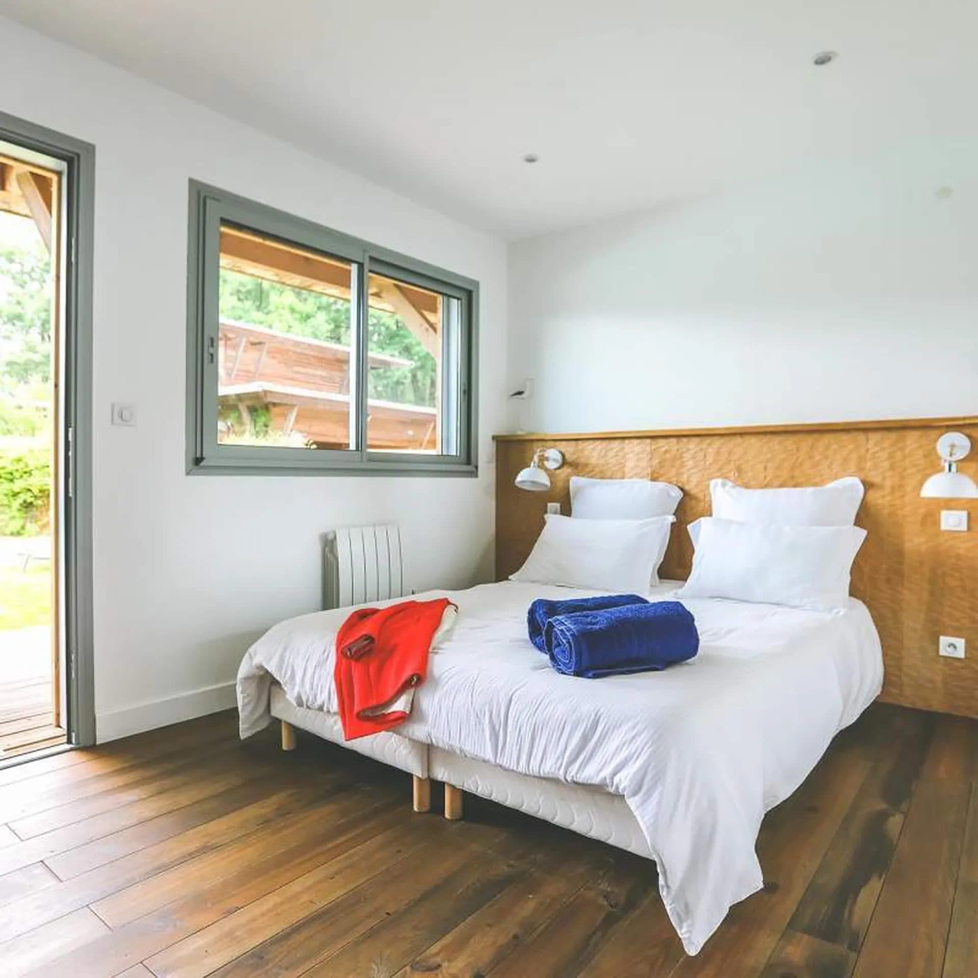Chambre d'hôtes avec tête de lit en bois, linge blanc et fenêtre sur le jardin