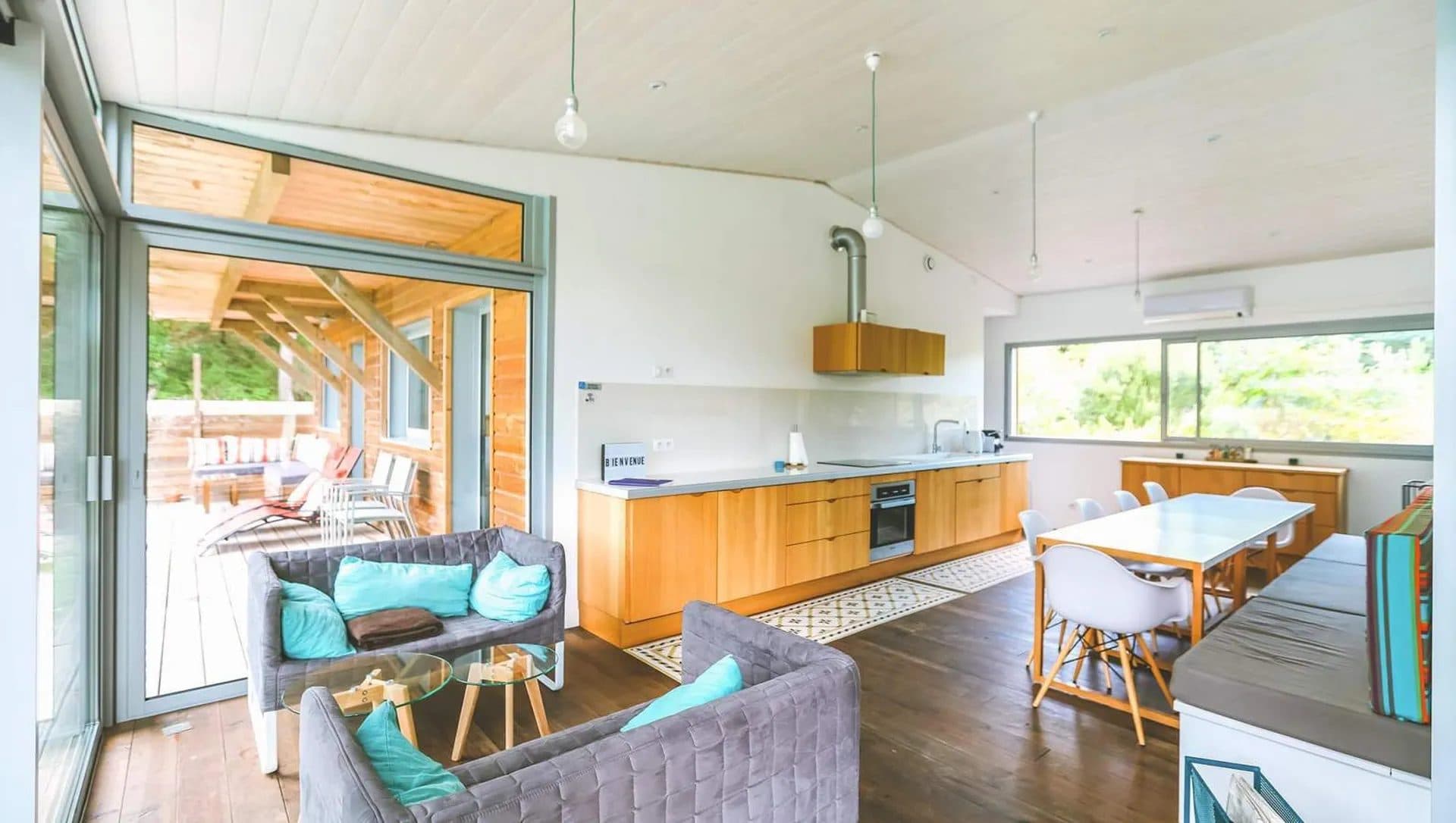 Séjour ouvert sur la terrasse par de larges baies, cuisine en bois clair et plafond lambrissé
