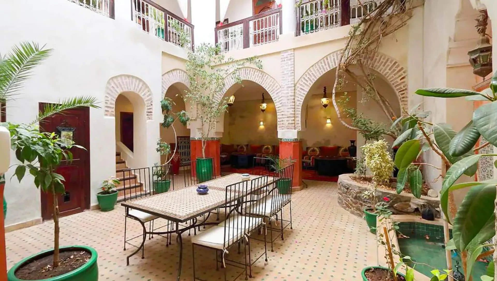 Patio de riad avec arcades blanches, zelliges au sol et plantations en pots
